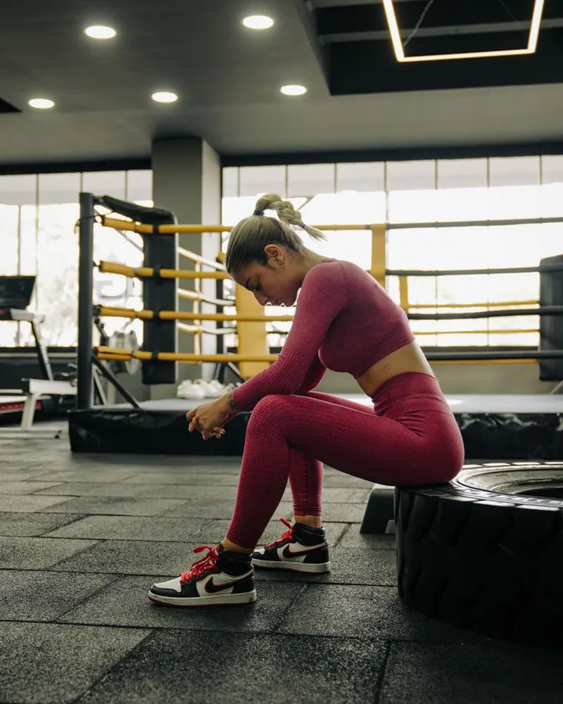 Mulher de roupa de treino sentada num pneu da academia, descansando entre uma série e outra