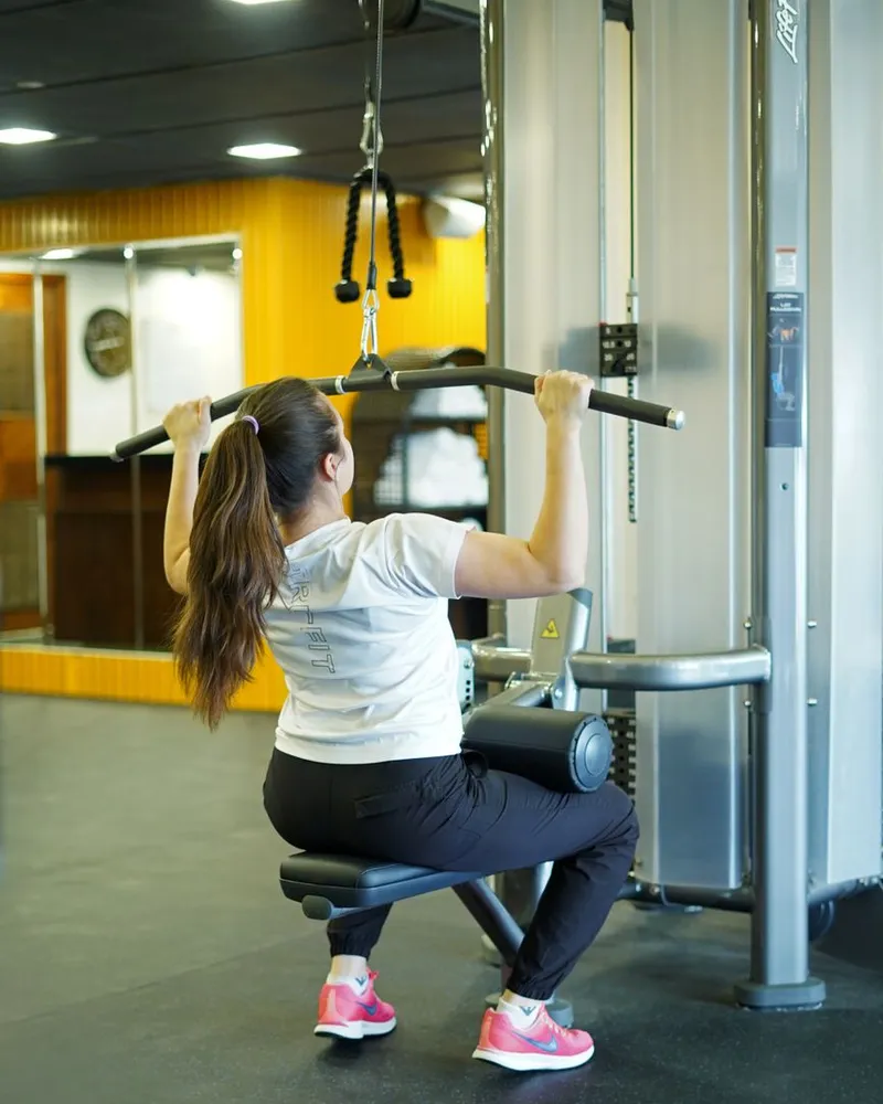 Mulher puxando a barra no puxador alto da academia