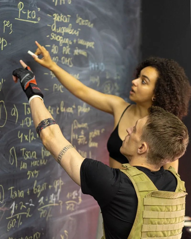 Professora escrevendo a ficha de treino no quadro para um aluno