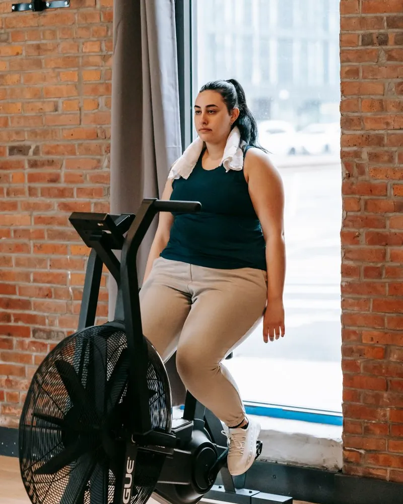 Mulher treinando na bike de ar da academia, perto da janela