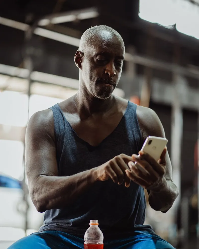 Homem conferindo o treino do dia no celular dentro da academia